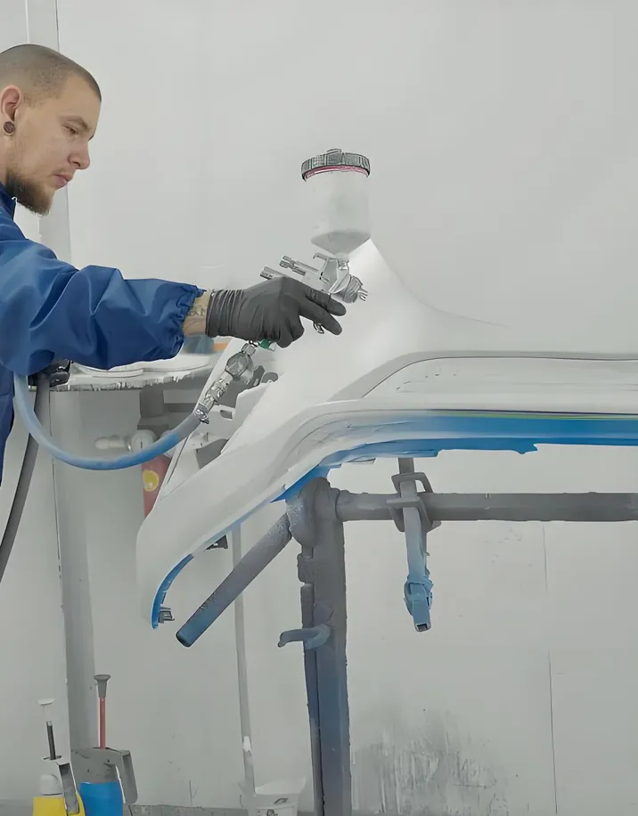 Painter in a paint booth spraying a bumper on a stand