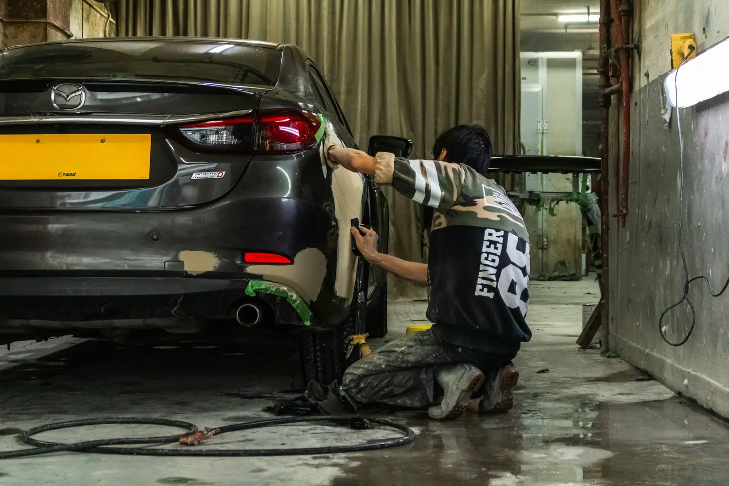 Technician preparing the rear of a grey car for paint