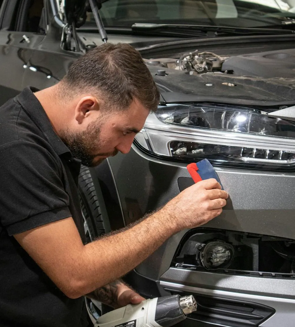 Technician sanding the bumper beside a headlight