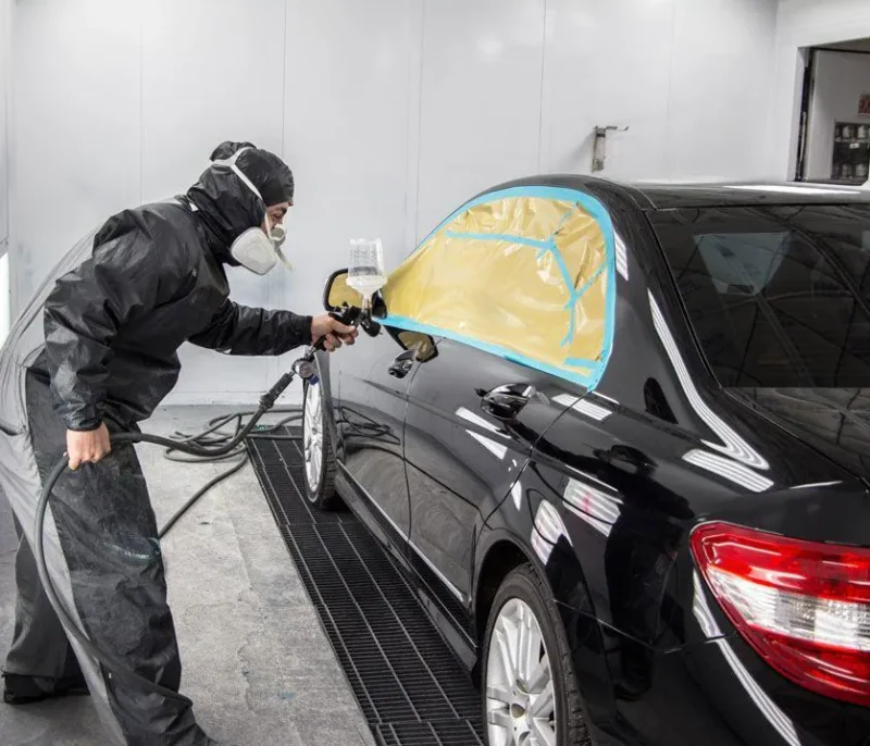 Painter refinishing a black car in a paint booth