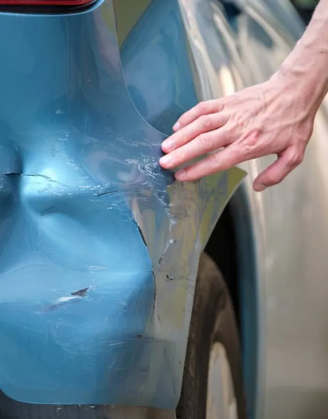 Hand pointing at a large dent in a light blue car panel