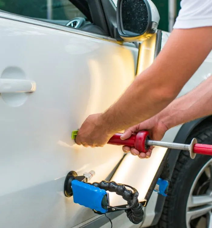 Technician using a paintless dent repair tool on a white car door