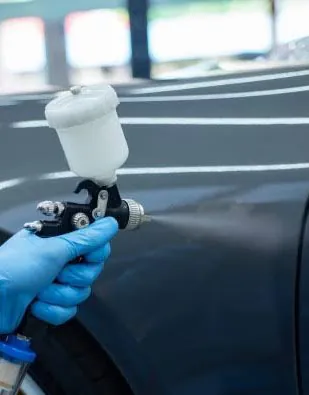 Gloved hand holding a spray gun over a car panel