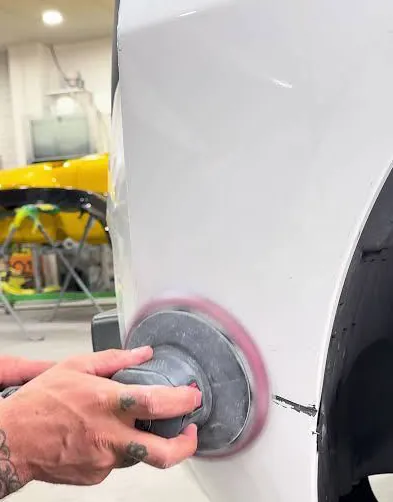 Technician sanding a small area of a white car body
