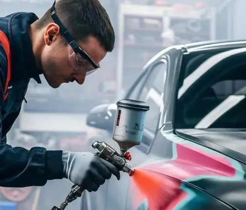 Technician in safety glasses spraying paint on a car