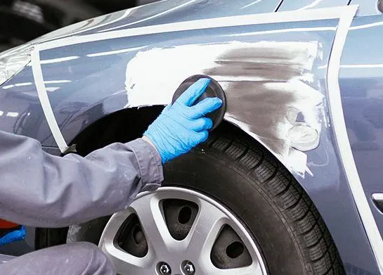 Technician sanding the wheel arch of a silver car